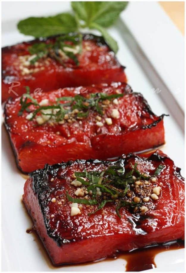 Watermelon steak, thick dark glazed slabs of seared watermelon laid in a row on a white platter with mint