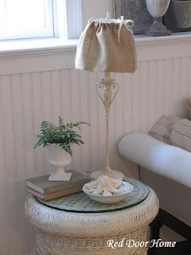 Round side table with a lamp wearing a natural burlap shade slipcover, above a stack of books and a white bowl
