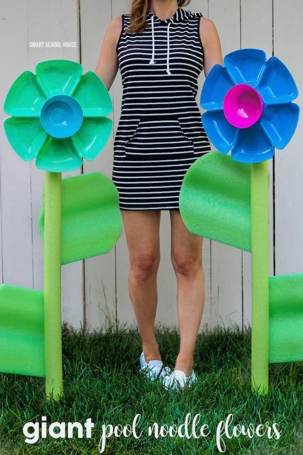 Giant pool noodle flowers graphic with two tray petal flowers in grass beside a woman in a striped dress