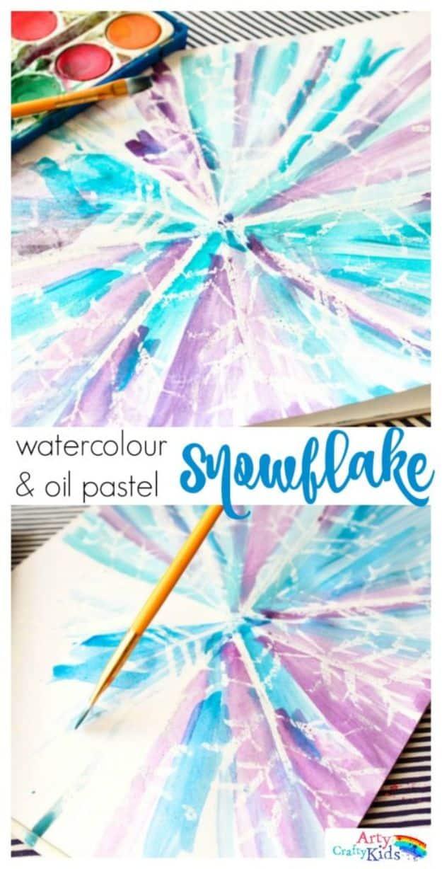 Watercolour snowflake in blue and purple revealed over white oil pastel lines, with a paint palette and brush