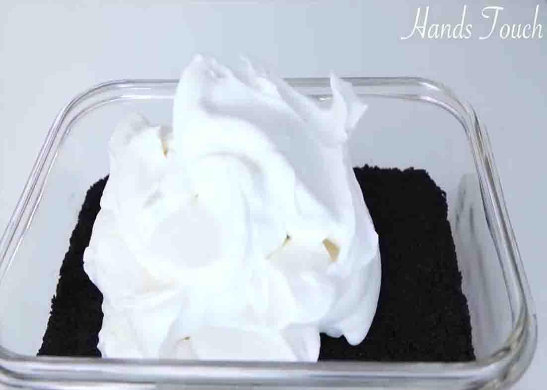 Adding the cream cheese mixture over the crushed Oreo cookies
