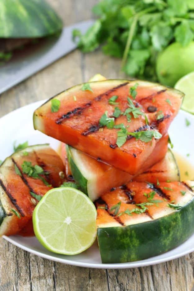 Cilantro lime grilled watermelon wedges with dark grill marks on a plate with lime halves and cilantro