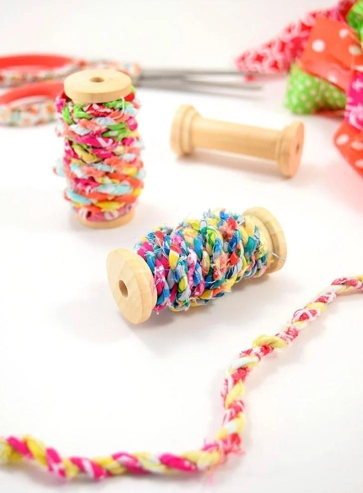 Handmade fabric scrap twine in bright prints wound onto two wooden spools, with a loose length of twisted cord alongside