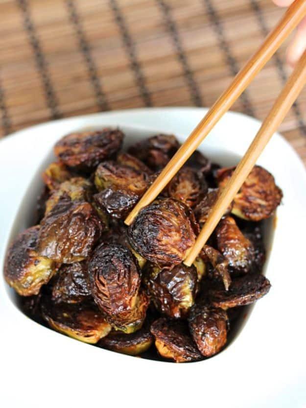 Crispy Asian brussels sprouts glazed dark with soy and maple in a white bowl, lifted with chopsticks
