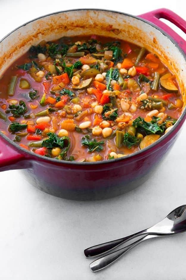 Kale and quinoa minestrone soup with white beans and vegetables in a red enameled pot with spoons beside