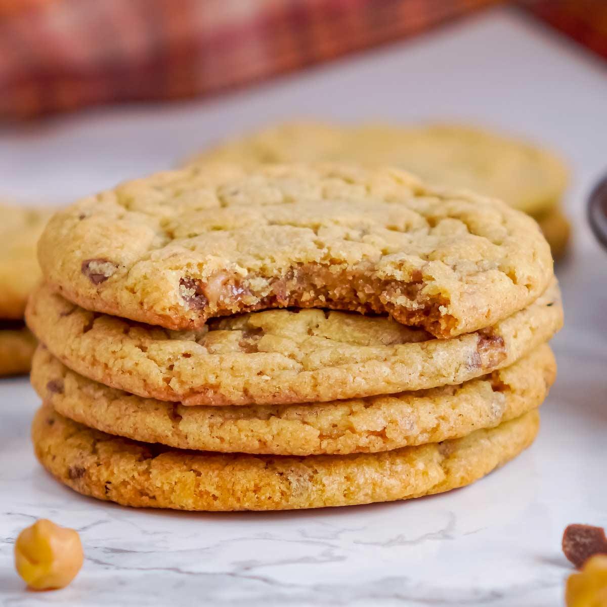 Stack of pumpkin cookies studded with toffee and caramel with one bitten cookie showing the soft center
