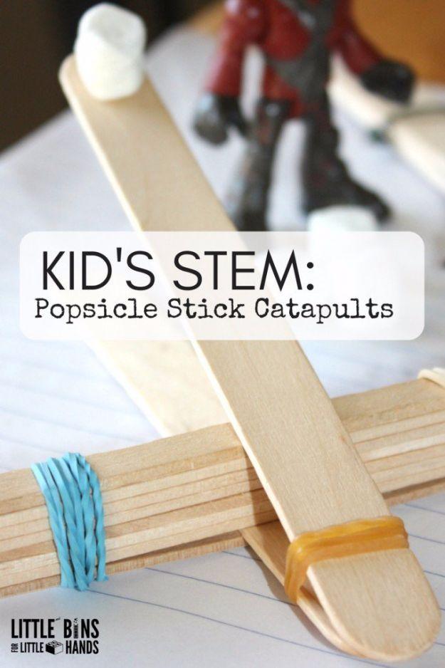 Popsicle stick catapult, craft sticks bound with blue and tan rubber bands, a marshmallow loaded and a toy figure behind