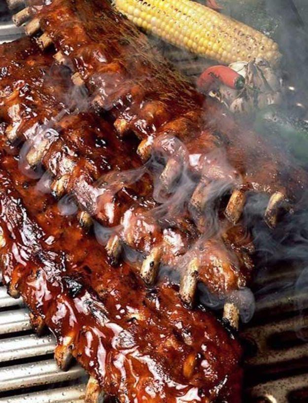 Coca Cola BBQ ribs, a glossy dark glazed rack cooking on a hot grill with smoke rising and corn on the cob beside it