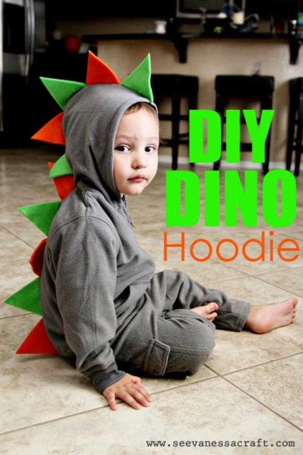 Sewing projects for boys dino hoodie in gray with green and orange felt spikes down the hood, worn by a seated toddler