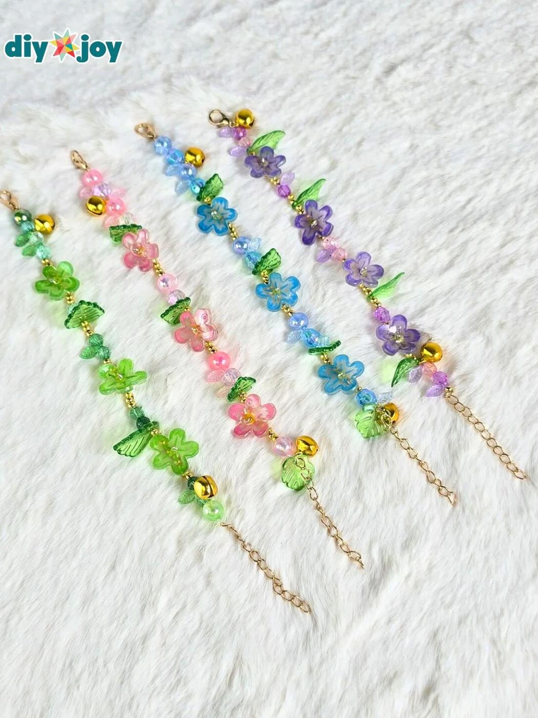 Four dainty shrink plastic flower bracelets in pink, blue, purple and green on gold chains laid in a row on white fur