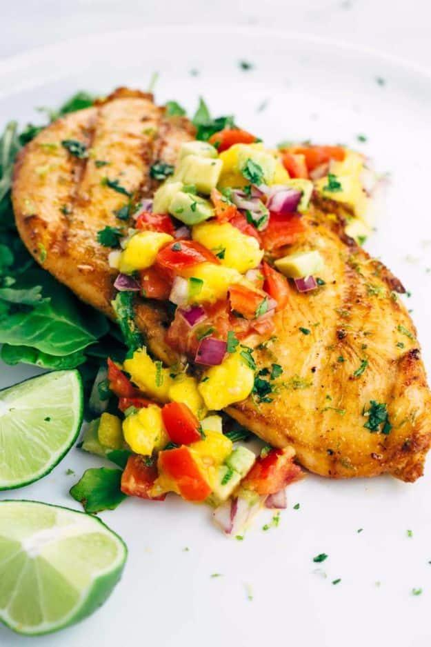 Grilled tequila lime chicken breast on a bed of greens topped with mango avocado salsa and lime wedges