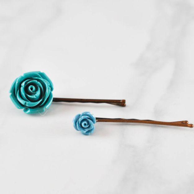 Two brown bobby pins with teal and pale blue resin flower cabochons glued to their tips, on white marble