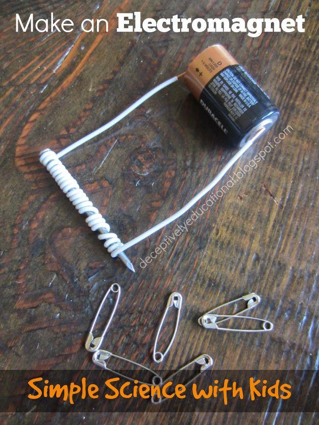 Make an electromagnet, a nail wrapped in coiled white wire beside a D cell battery on dark wood with safety pins below