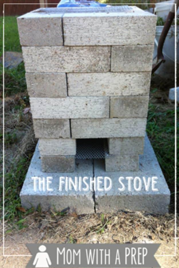 Rocket stove built from stacked grey concrete blocks with a fuel opening at the base, standing on bare ground