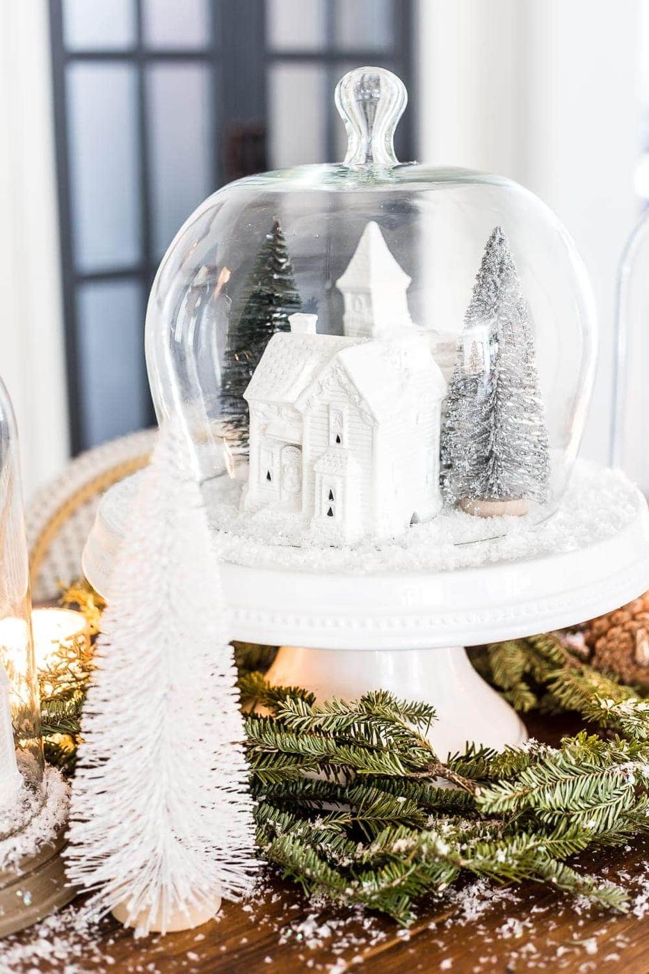 Two glass dome cloches with white painted village houses, bottle brush trees and fake snow on weathered wood bases
