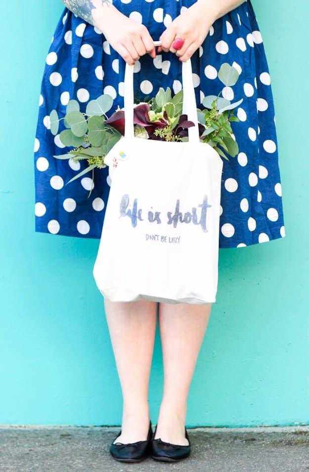 A natural canvas tote pressed with a black iron on graphic, hanging from a wooden peg against a plain white wall