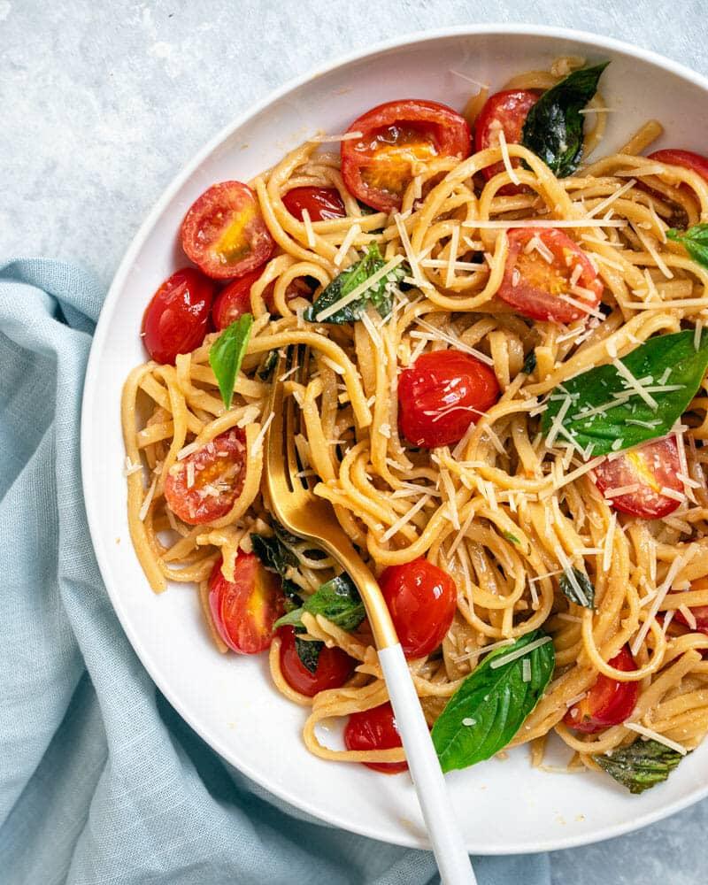 Tomato basil pasta, spaghetti tossed with halved cherry tomatoes and fresh basil leaves on a white plate