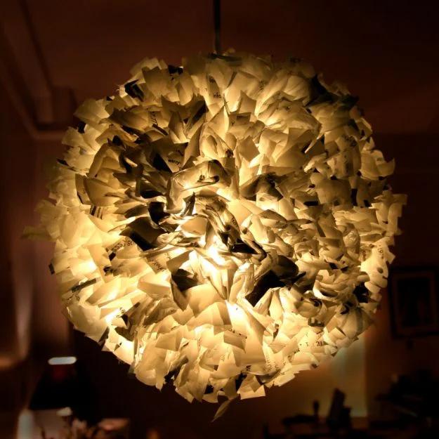 Pendant light made from plastic bag strips threaded through a mesh sphere, lit and glowing warm in a dim room