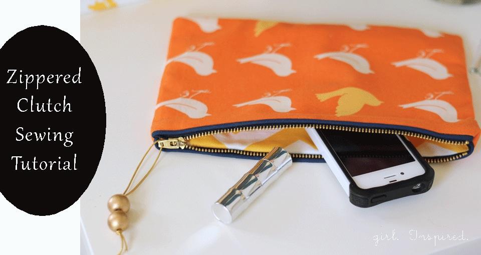 An orange zippered clutch printed with white and yellow birds, unzipped to show a phone and a lipstick inside