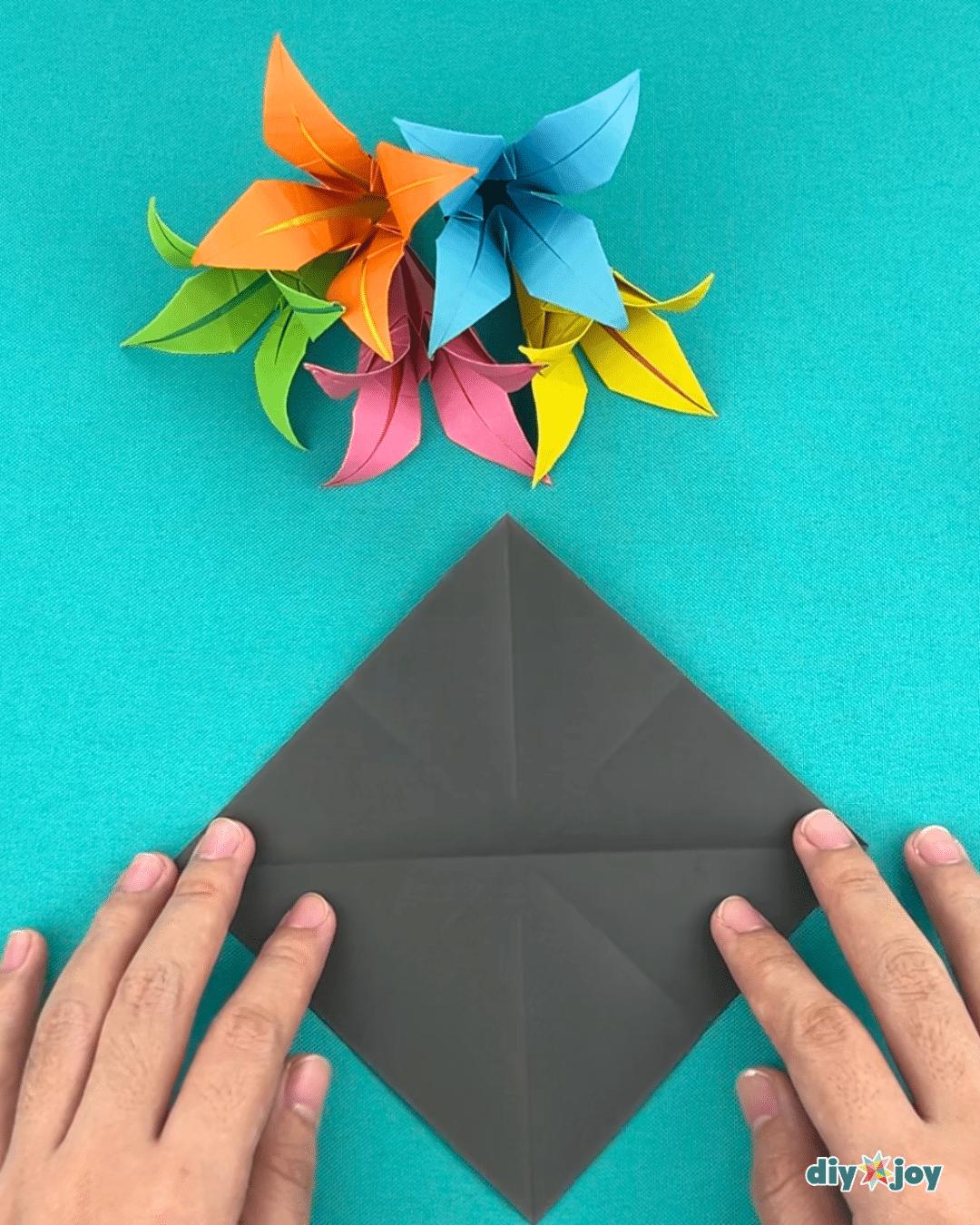 Easy paper craft in progress, the folded square being collapsed toward the center for a homemade paper lily
