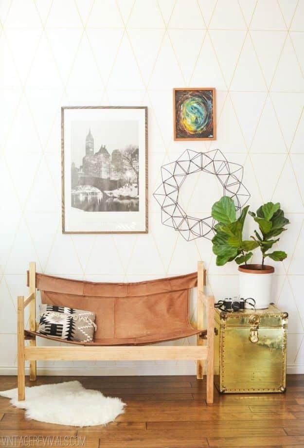 Wooden safari sling bench with a tan leather seat and back, patterned cushions, beside a brass trunk and fiddle leaf fig