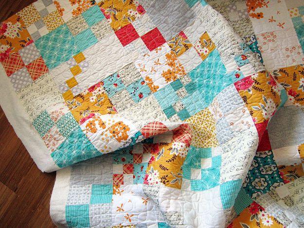 Penny patch quilt with small aqua, mustard and coral four patches among white squares on a wood floor