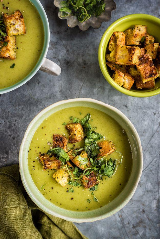 Two bowls of bright green spinach coconut and zucchini soup topped with golden garlic and herb croutons