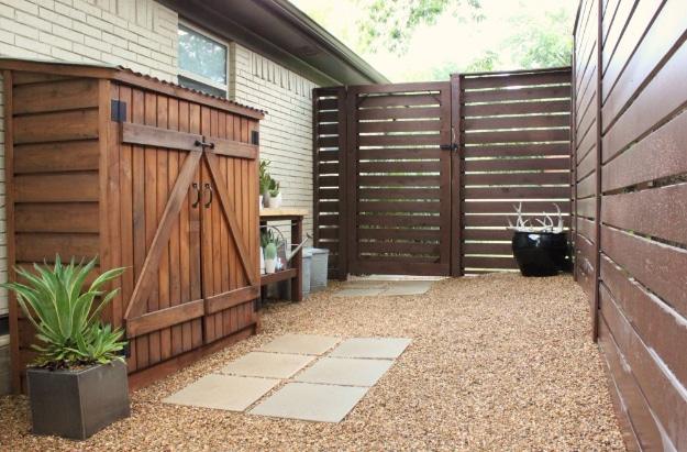 Modern fence DIY, a dark stained horizontal slat fence and matching gate along a narrow gravel side yard beside a house