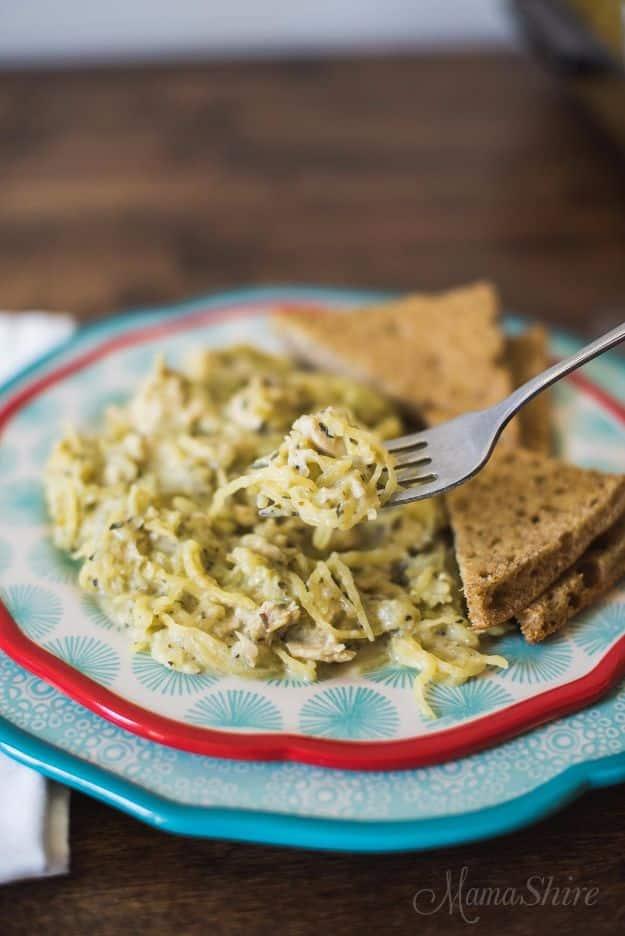 Baked spaghetti squash alfredo with a fork resting in it on a teal and red plate beside two slices of dark bread