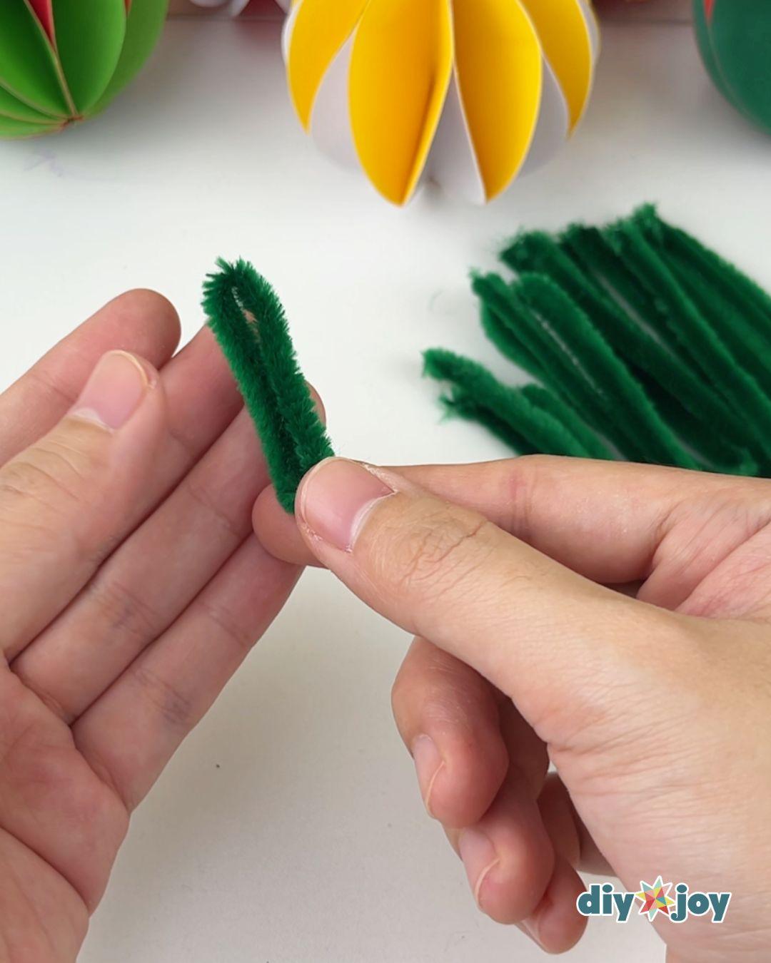Kids Christmas Crafts - fingers pinch a short green pipe cleaner segment folded in half with more cut pieces piled behind