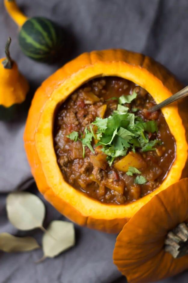 Paleo pumpkin chili served inside a hollowed orange pumpkin, topped with fresh cilantro on a grey cloth