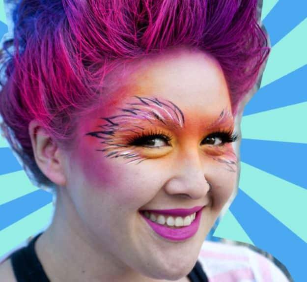 Lorax Halloween makeup with orange face paint, black whisker lines, pink cotton candy hair and fuzzy brows