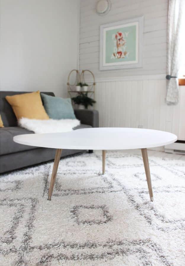 Kidney shaped white gloss coffee table on three pale tapered legs on a patterned shag rug beside a grey sofa