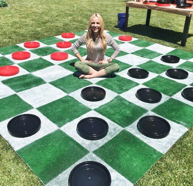 DIY lawn checkers board on green astro turf grass with oversized red and black checkers made from painted bucket lids