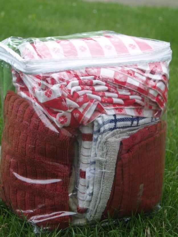Camping bedding storage, a red and white quilt and folded towels packed in a clear zip bag on green grass
