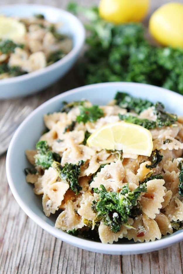 Goat cheese lemon pasta with kale in a blue bowl with a lemon wedge on top and fresh lemons behind it