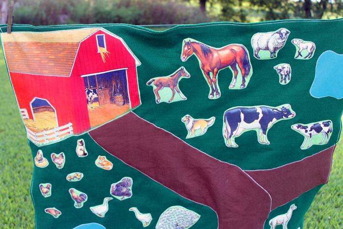 A green felt farm play mat with brown felt roads, a blue pond and fabric barn, horse, cow, sheep and chicken cutouts