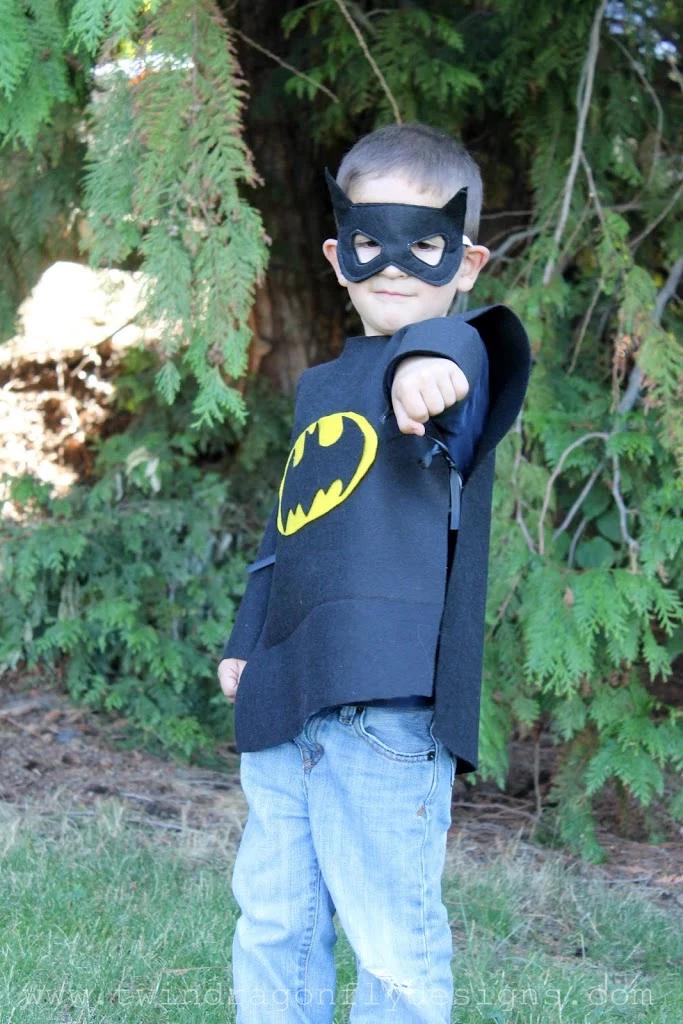 Child wearing a black felt Batman superhero costume with a cape and mask, standing outdoors with one fist raised