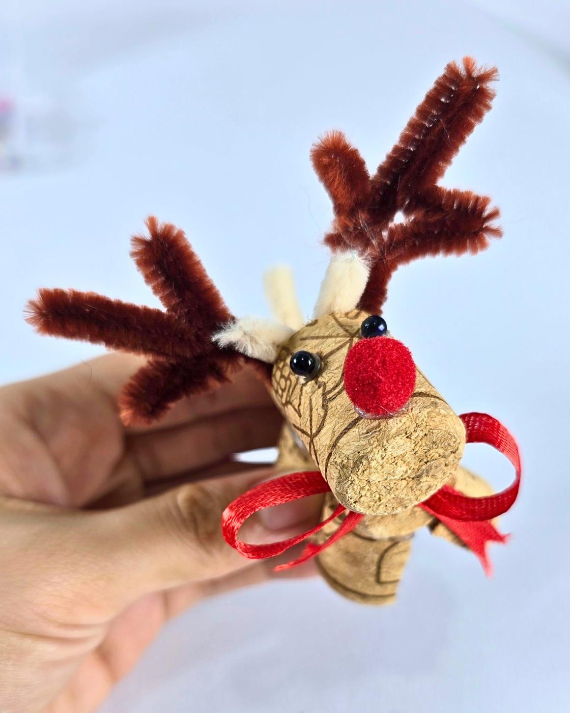 DIY Crafts - a hand holding one finished cork reindeer with a red pom pom nose and white tipped antlers