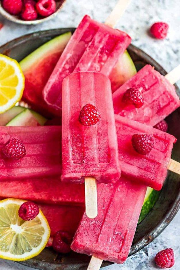 Watermelon raspberry popsicles lying in a dark metal tray with raspberries, lemon slices and watermelon