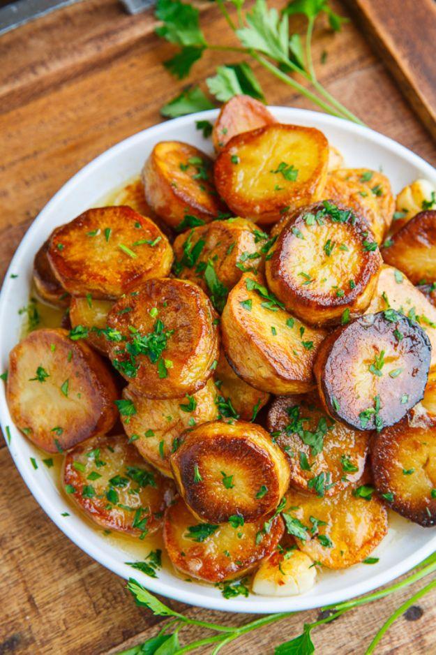 White plate of thick browned melting potato rounds scattered with chopped parsley on a wooden serving board