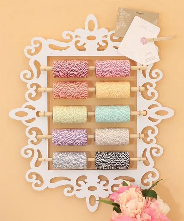 Ornate white cut out frame fitted with wooden dowels holding rows of pink, green and striped twine spools