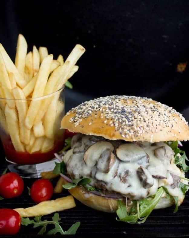 Mushroom Swiss cheese burger on a seeded bun with melted Swiss and mushrooms, fries stacked behind it