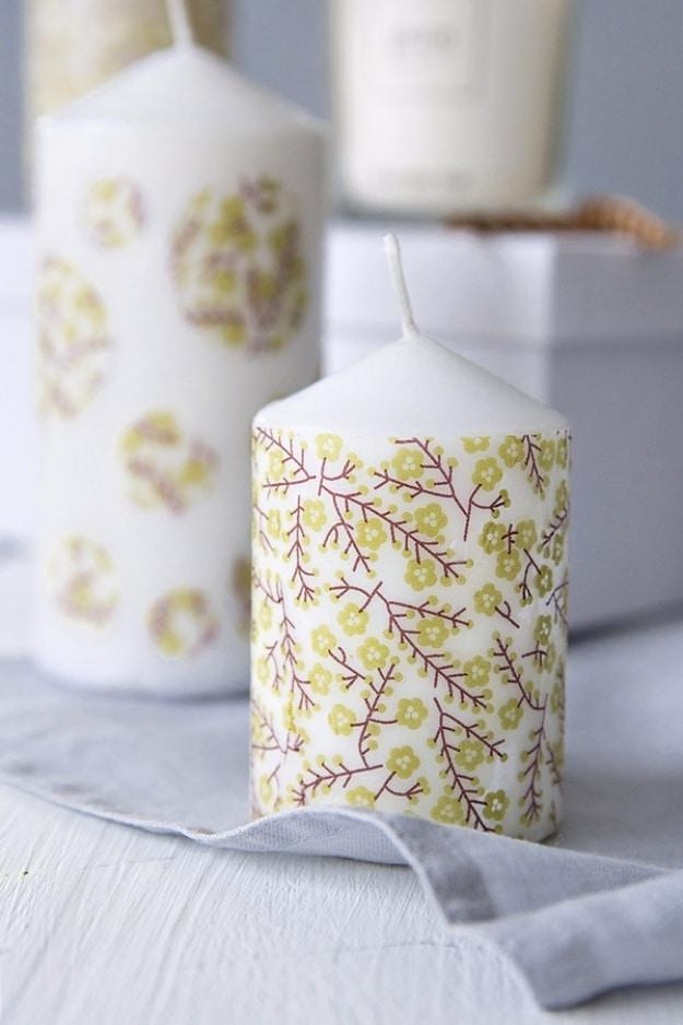 A cream pillar candle with a napkin motif melted into the wax low on the side, lit on a round wooden tray