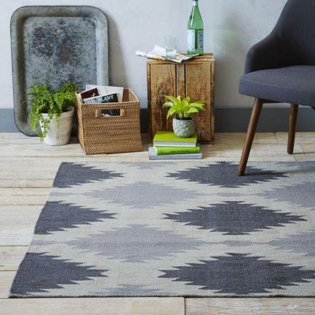 Gray and cream geometric painted rug on a wood floor in a room with plants, crates and a modern chair