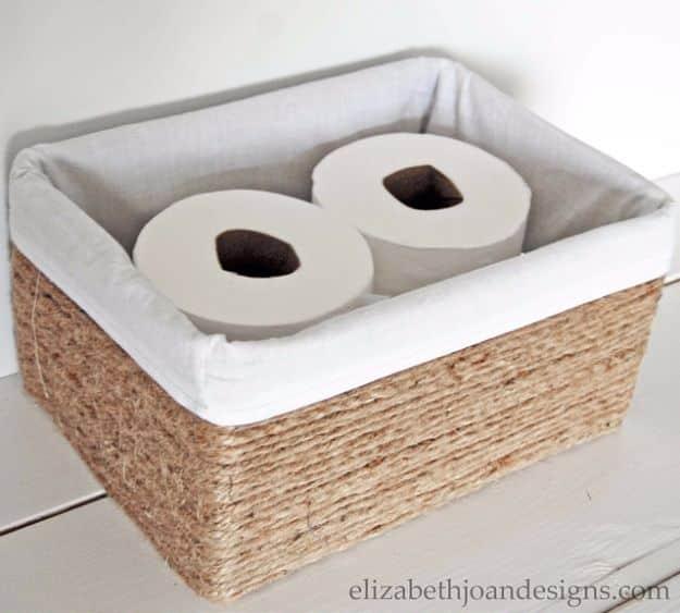 Cardboard craft rope wrapped basket with a natural linen liner holding rolls of toilet paper on a floor