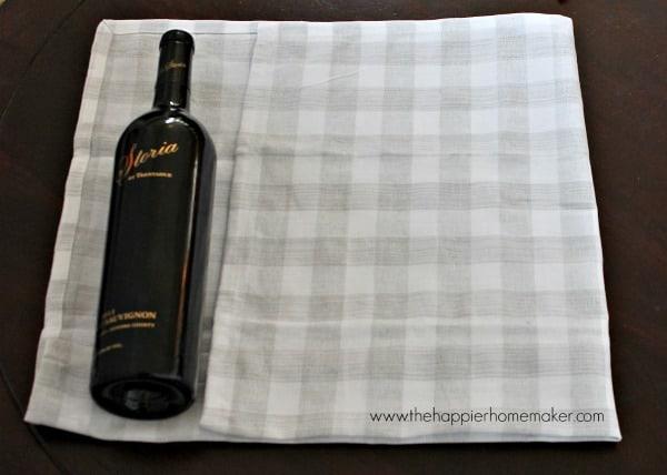 Wine bottle wrapped in a patterned tea towel, pinned at the edge and tied at the neck with a red ribbon as a hostess gift