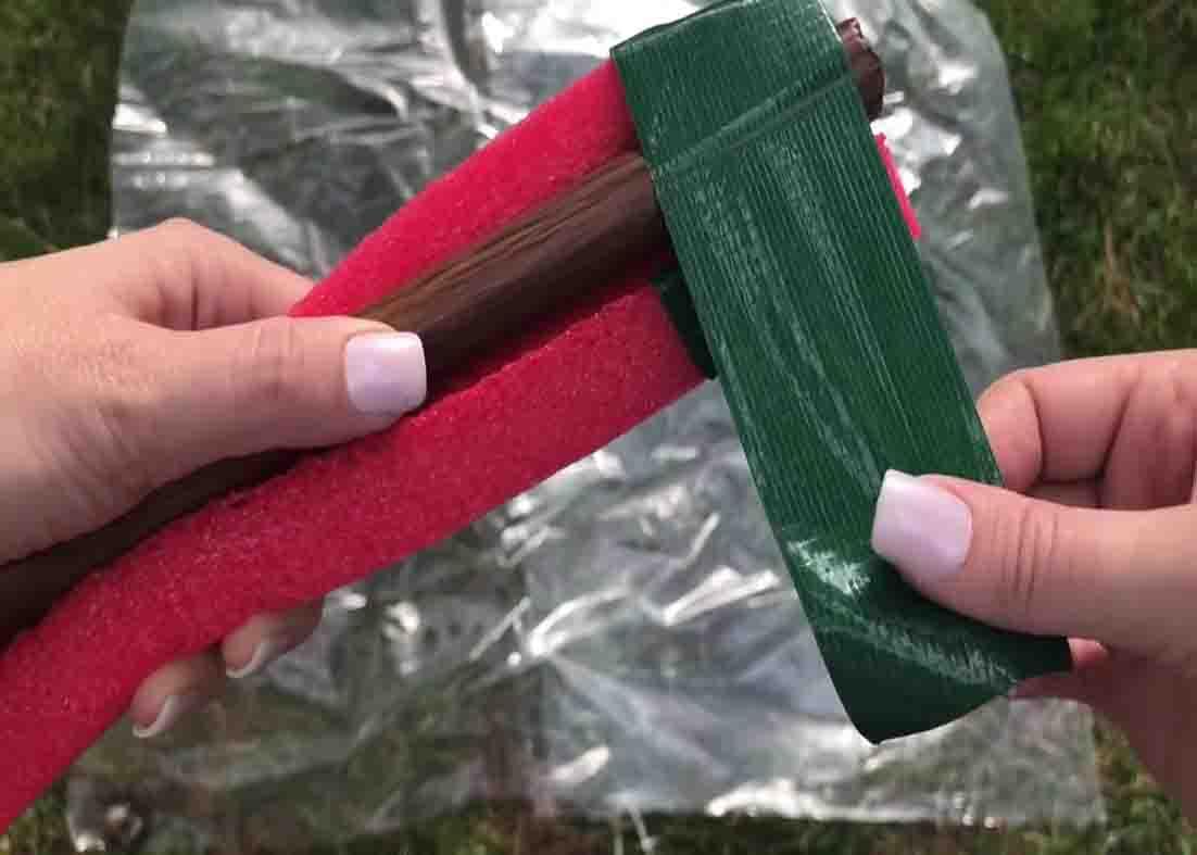 Taping the broomstick and the pool noodle together to make the DIY spiral topiary