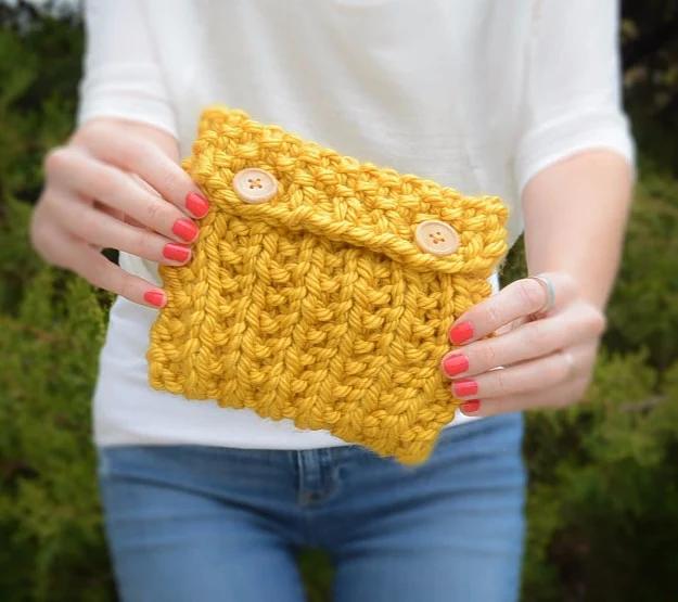 Mustard yellow chunky knit pouch with two round wooden buttons, held in both hands against a white shirt and jeans