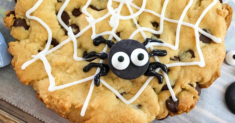 Jumbo chocolate chip spiderweb cookie decorated with white icing rings and a dark chocolate spider for Halloween